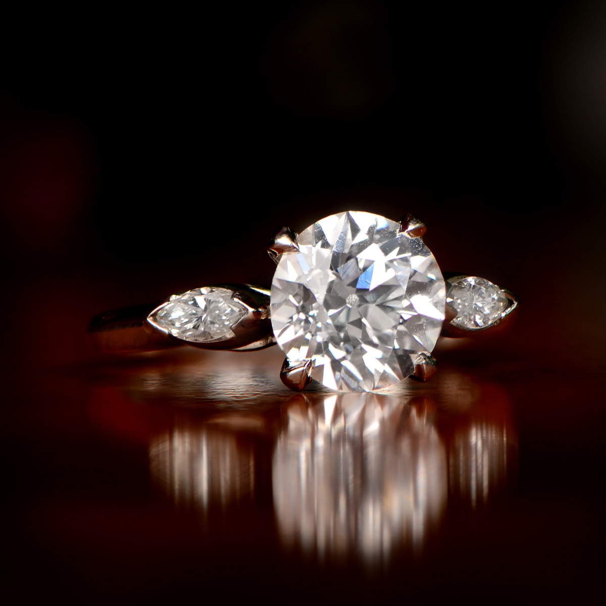 An engagement ring with a large round diamond and two small diamonds on the sides, on a dark background