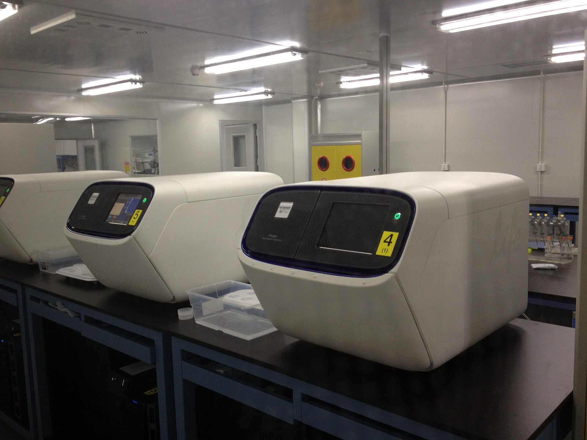 Several white DNA-reading machines on a table in a brightly lit laboratory