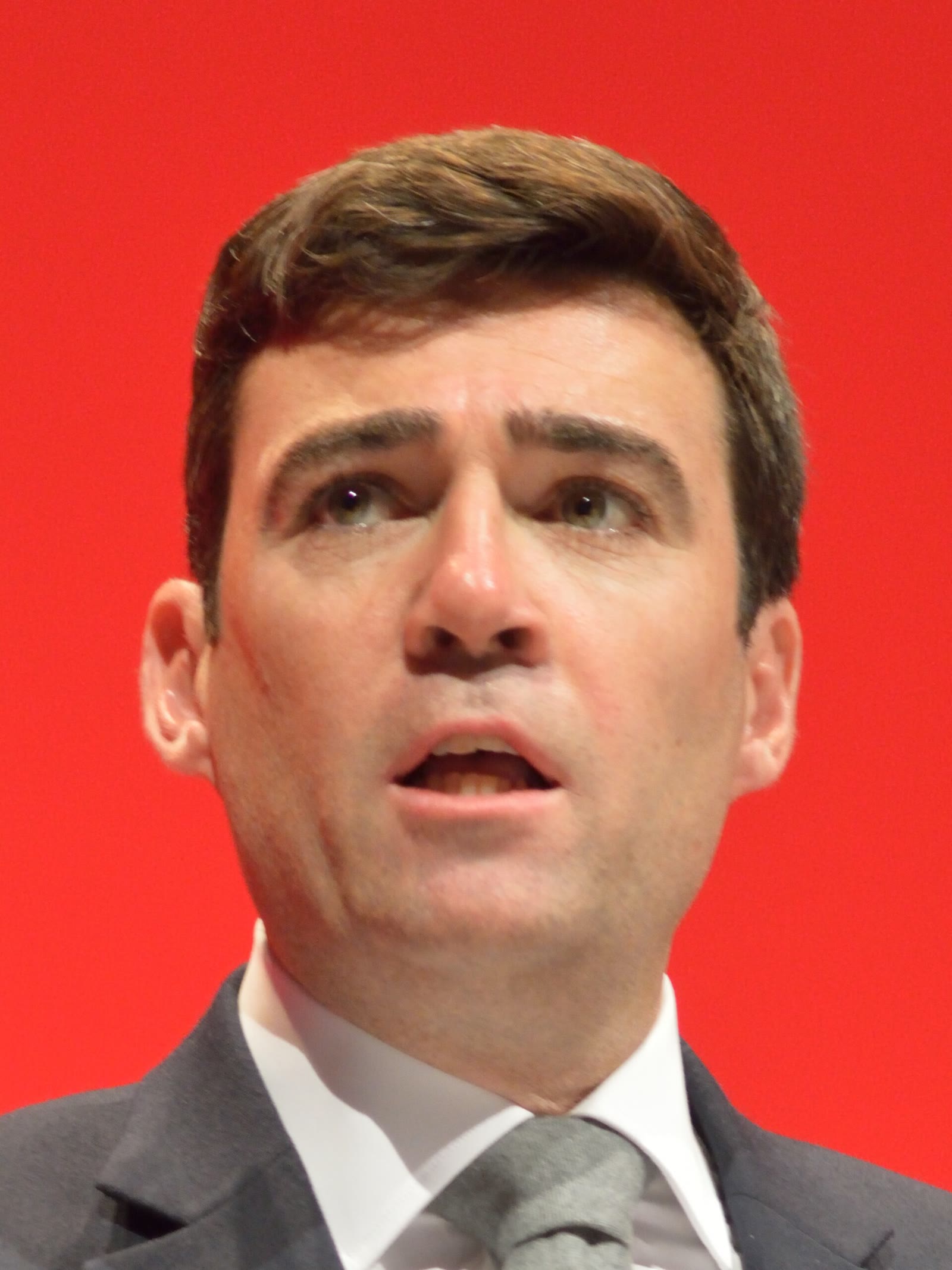 Andy Burnham hablando en un congreso del Partido Laborista, delante de un fondo rojo