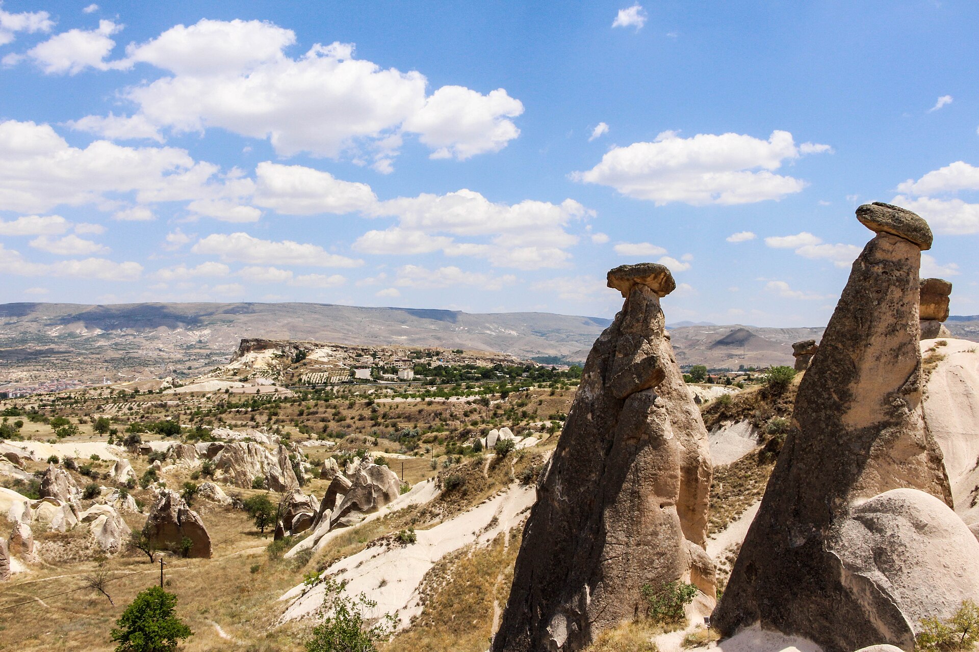 Two mushroom-shaped rock spires, the fairy chimneys, beside a valley in Cappadocia under a blue sky with clouds