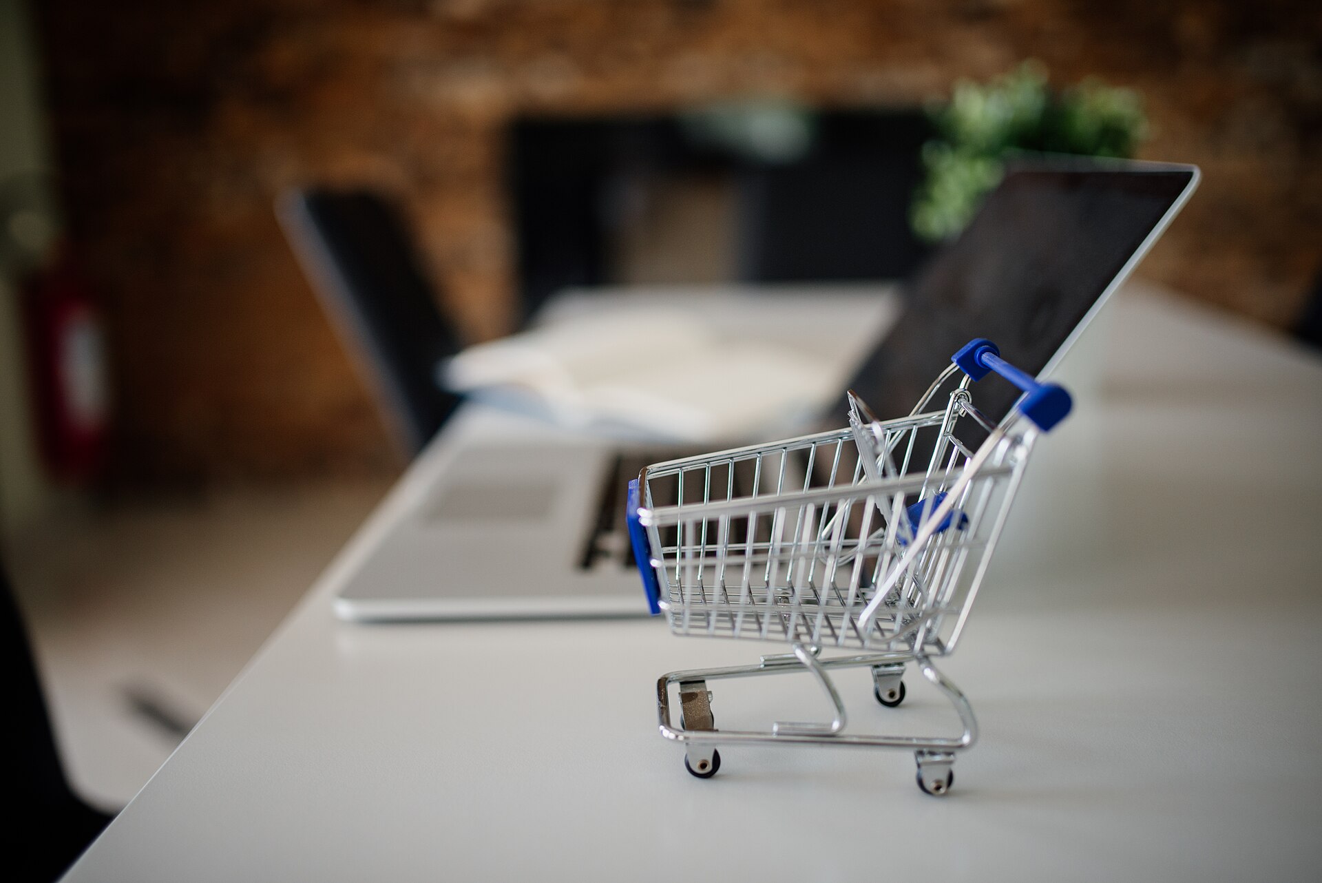 A miniature shopping cart on a white table, in front of an open laptop