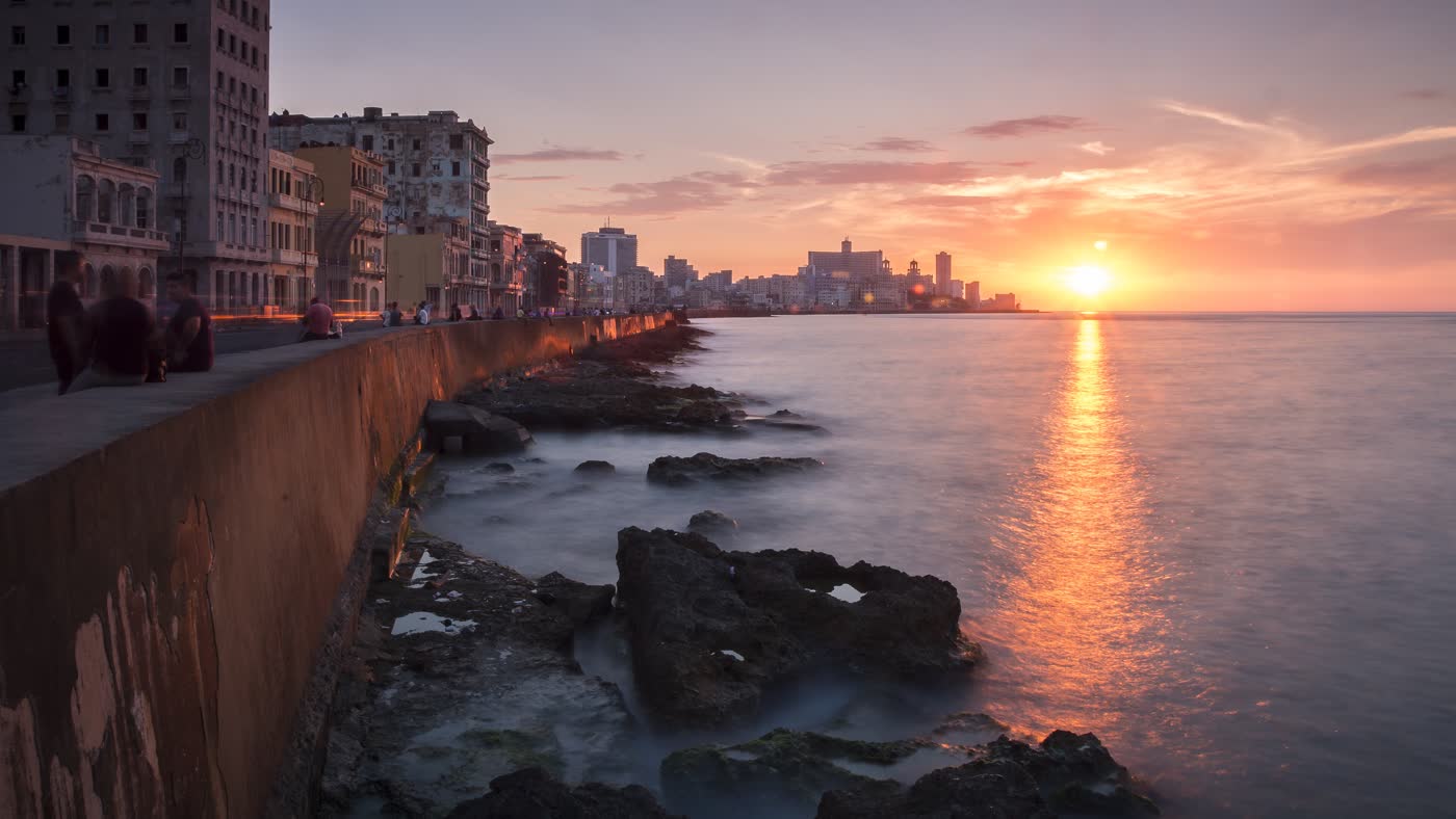 El malecón de La Habana al atardecer, con el sol sobre el mar y los edificios de la ciudad al fondo