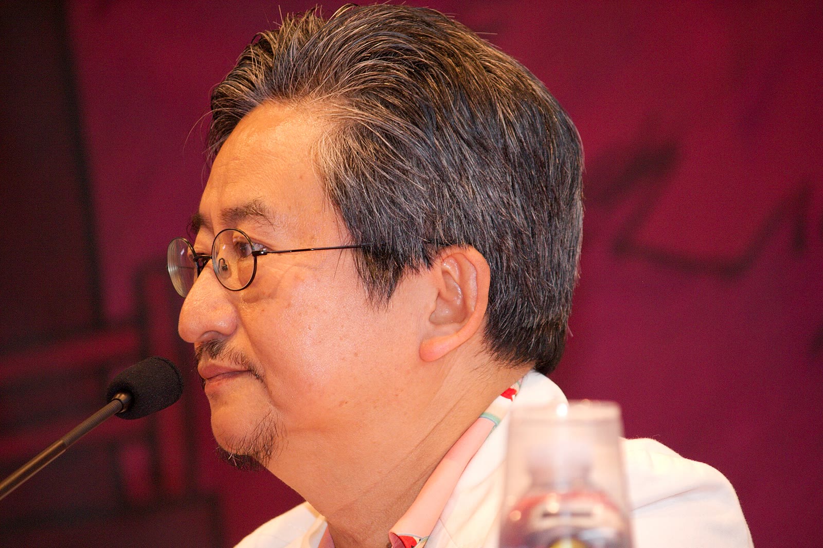Go Nagai, dibujante japonés con gafas, hablando a un micrófono durante una conferencia