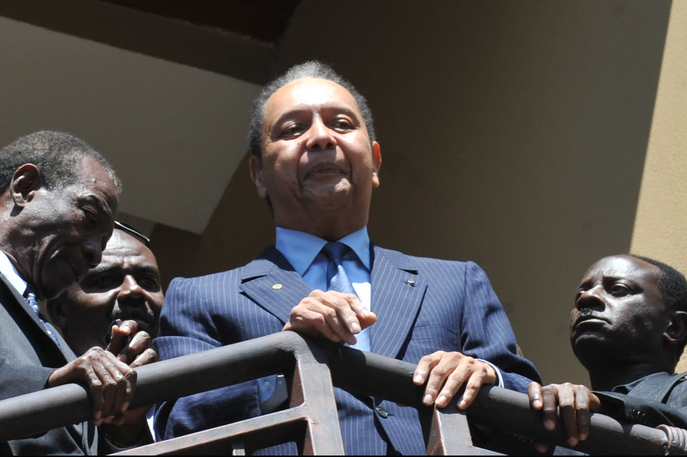 Jean-Claude Duvalier, con traje azul, saluda desde un balcón rodeado de otras personas