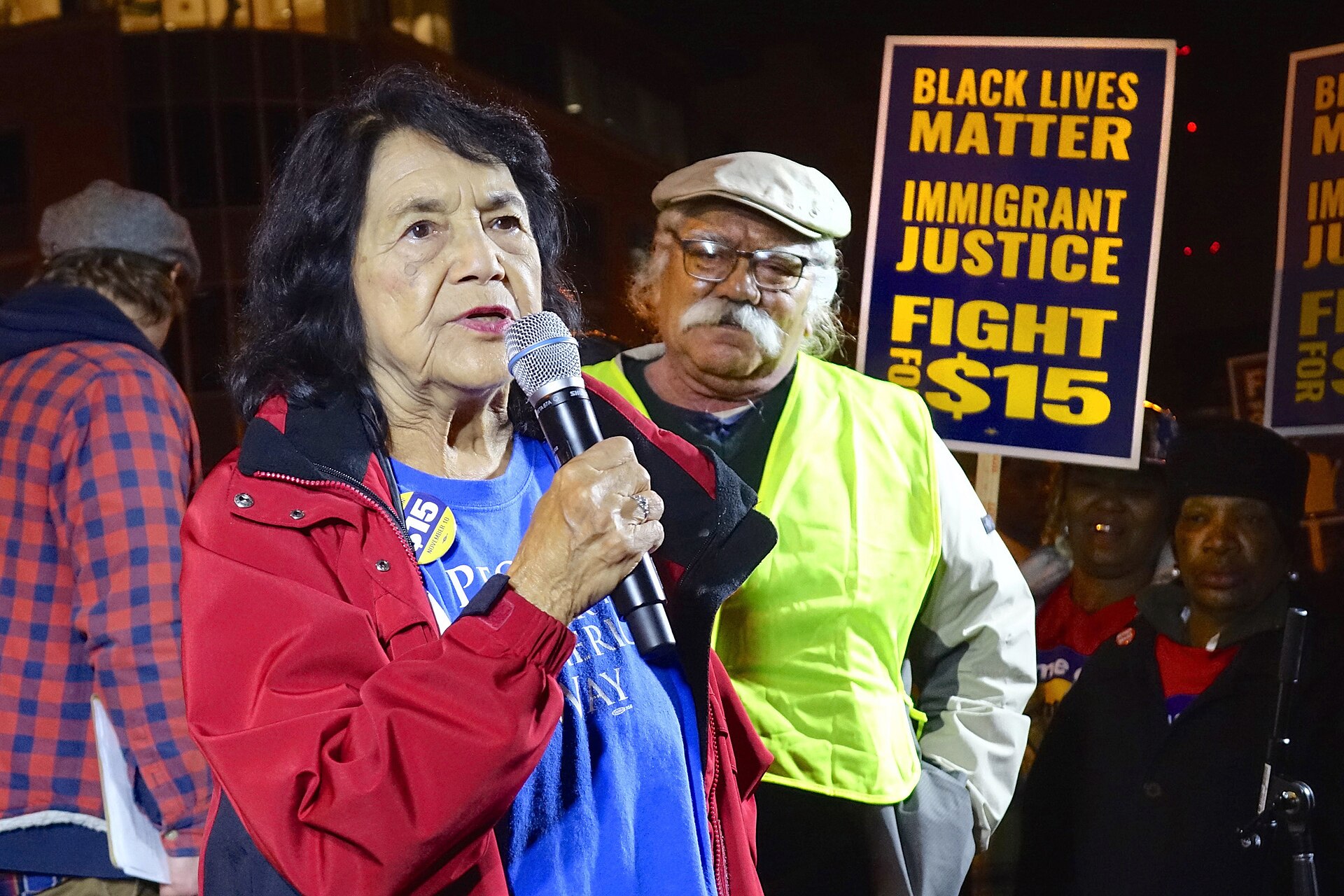 Dolores Huerta hablando con un micrófono durante una protesta nocturna de trabajadores
