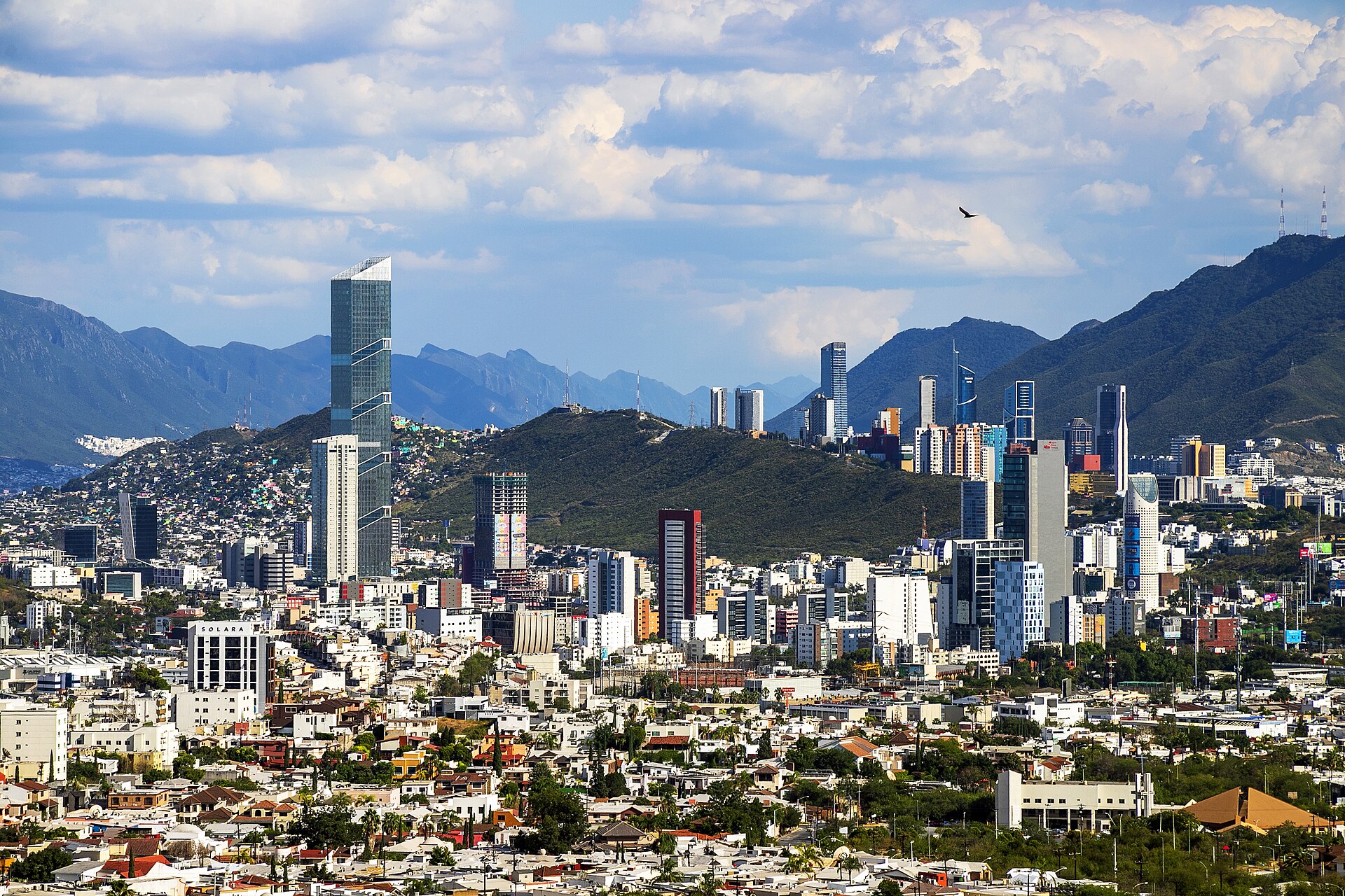 View of Monterrey's skyscrapers with green hills and mountains in the background under a cloudy sky