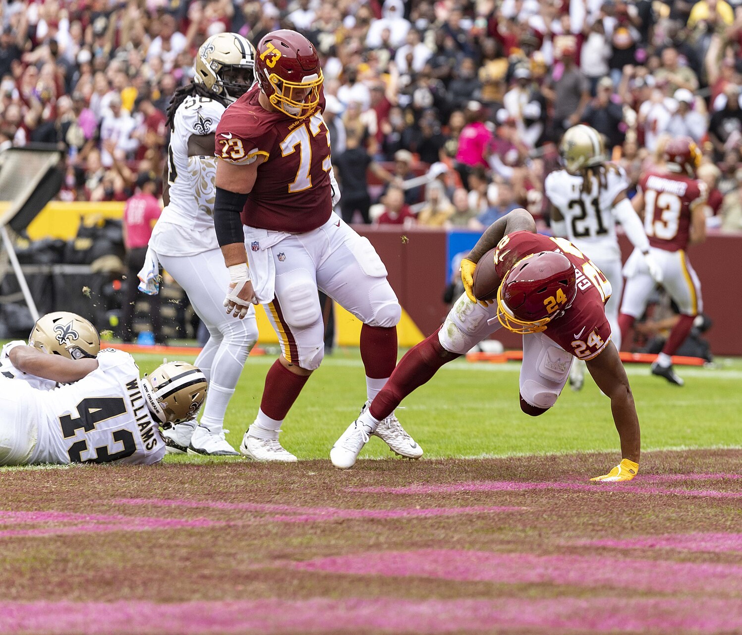 Football players in helmets, some in maroon and others in white, in the end zone in front of a packed stadium