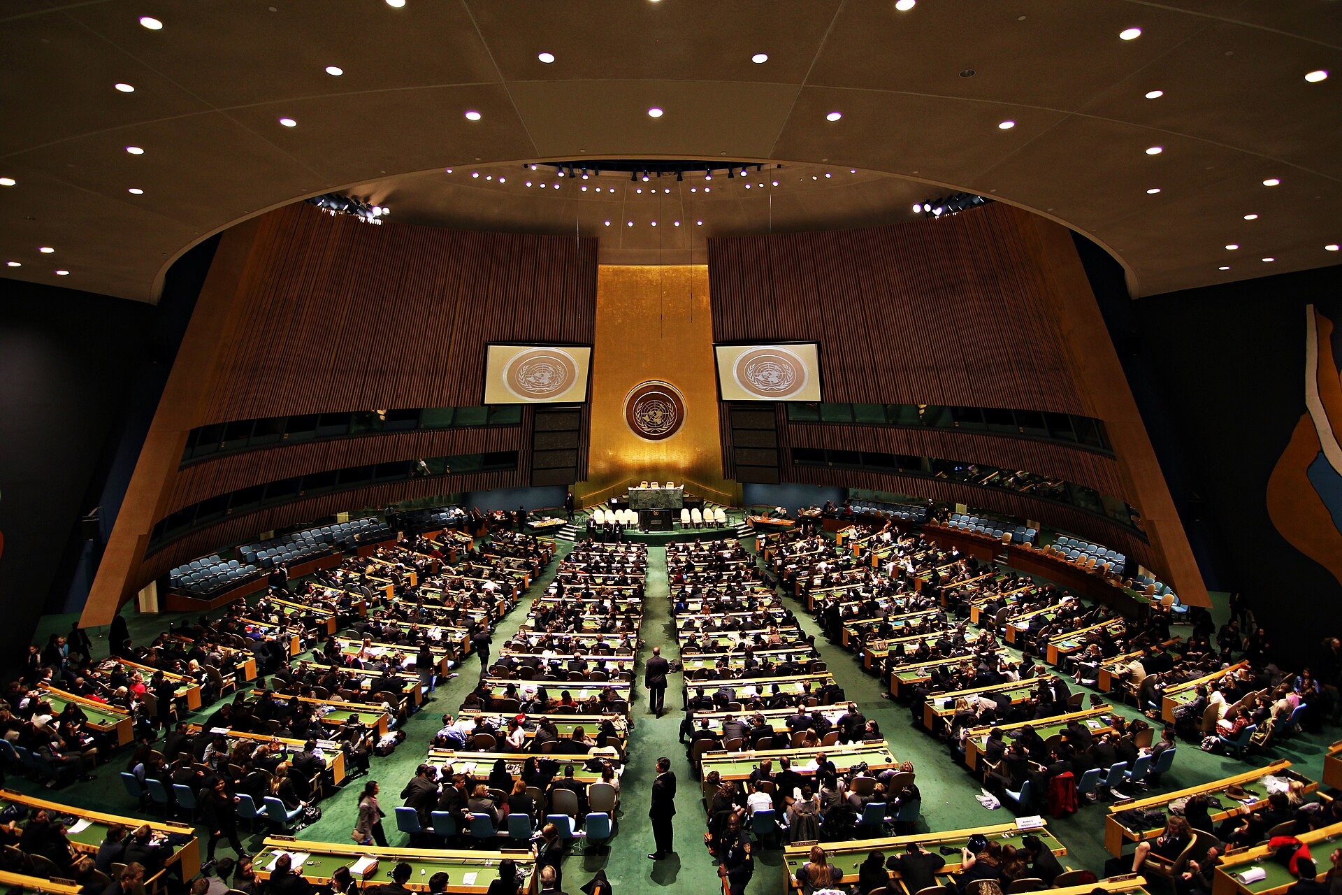 Gran salón de la Asamblea General de la ONU, en Nueva York, lleno de delegados y con el emblema dorado al fondo