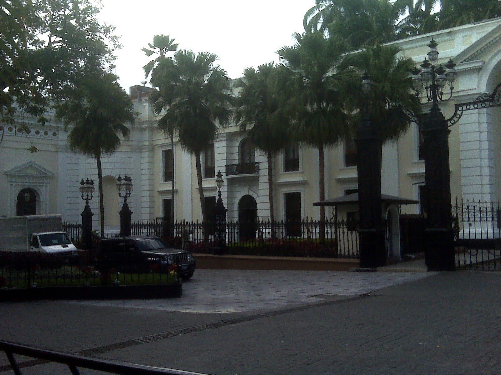 White building of the Federal Legislative Palace in Caracas, with palm trees and a fence in front