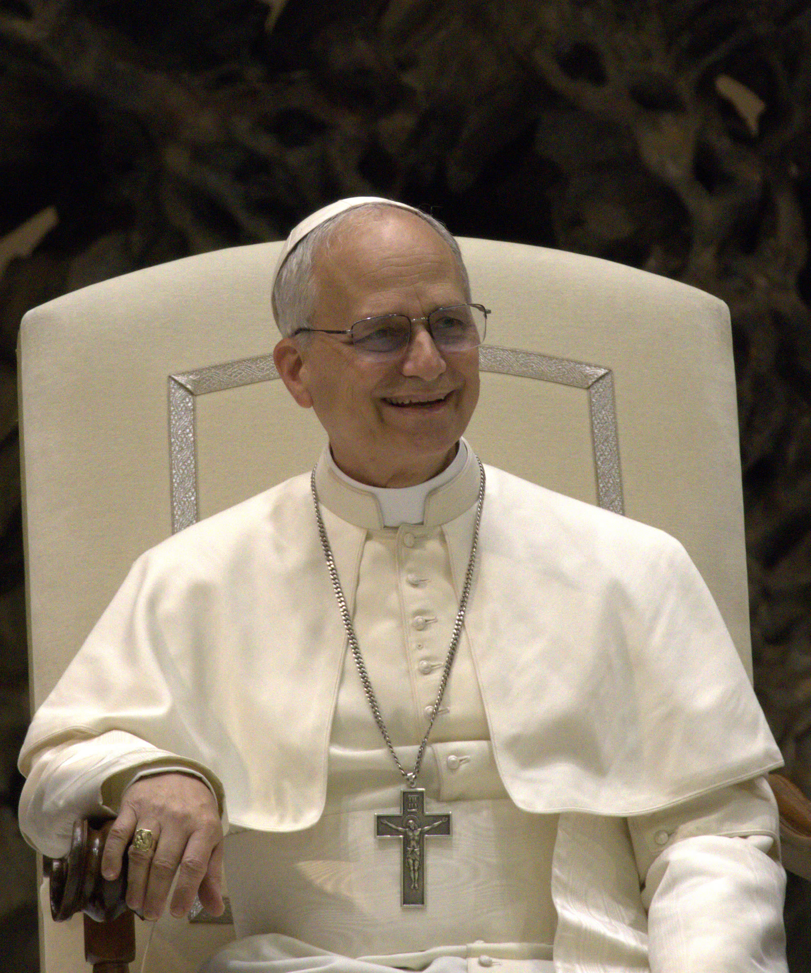 El papa León XIV, vestido de blanco, sonriendo sentado en un sillón