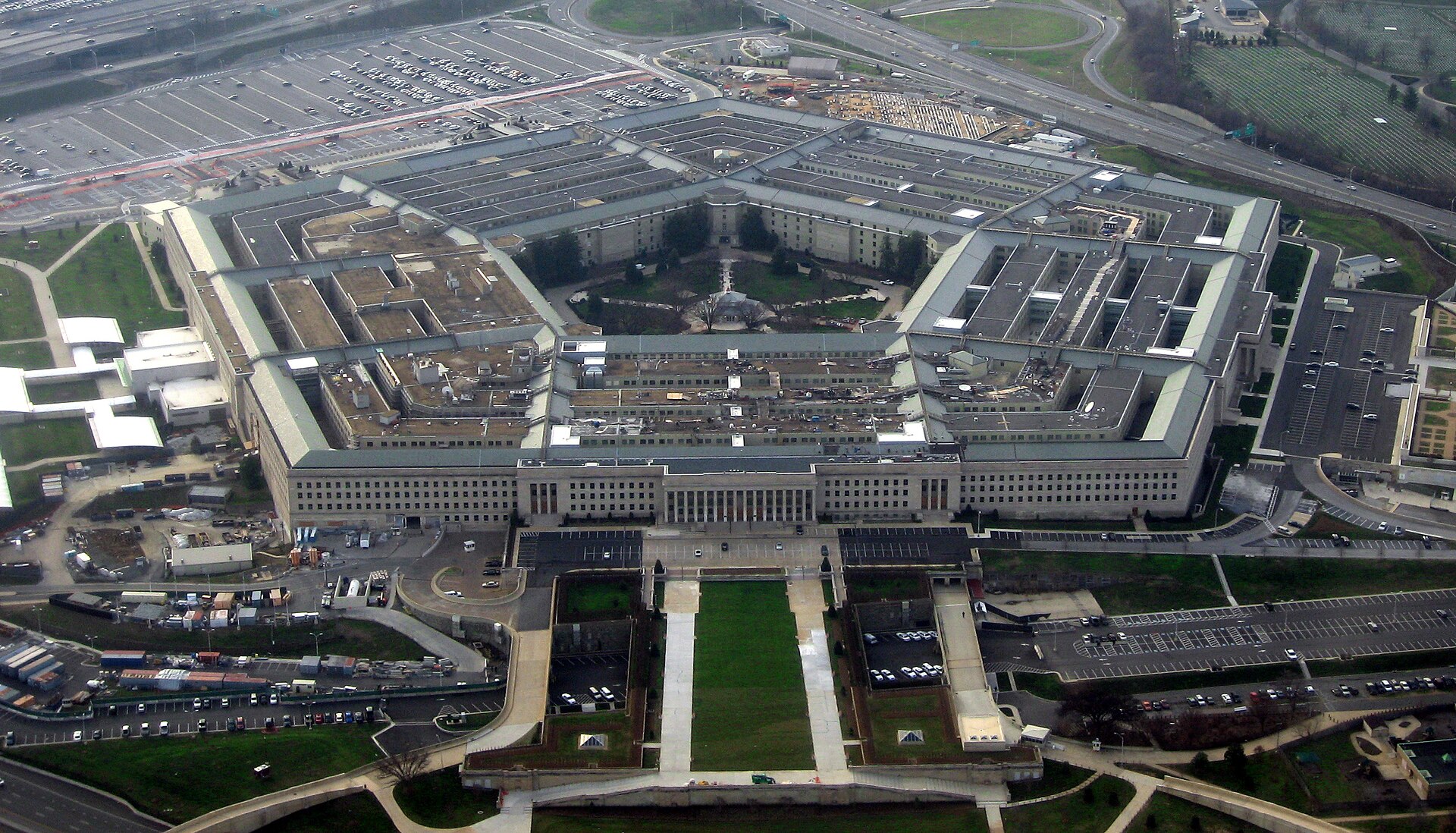 Aerial view of the Pentagon, a huge five-sided building with a green central courtyard, surrounded by parking lots and roads