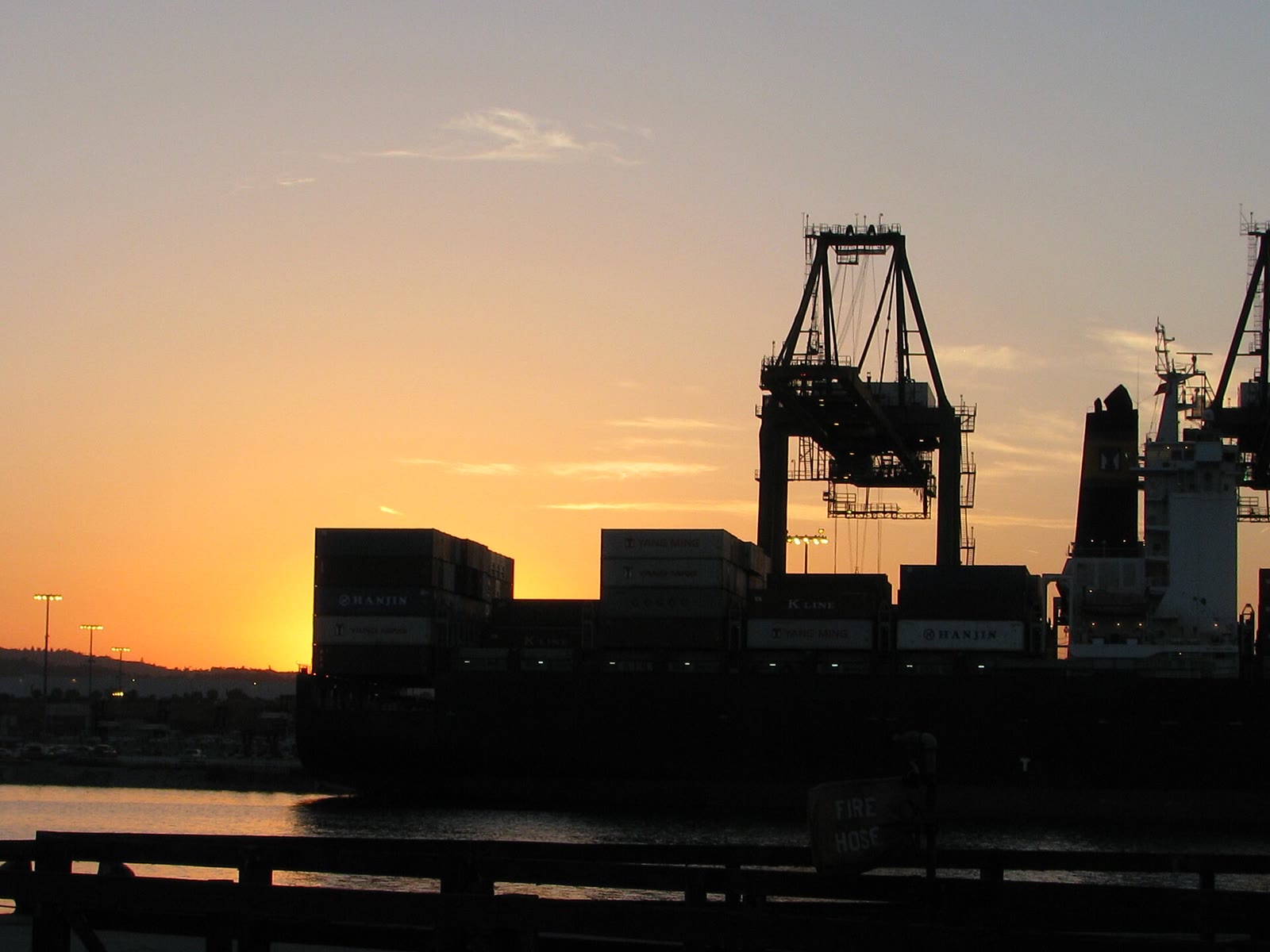 Silhouette of a container ship and a port crane at sunset