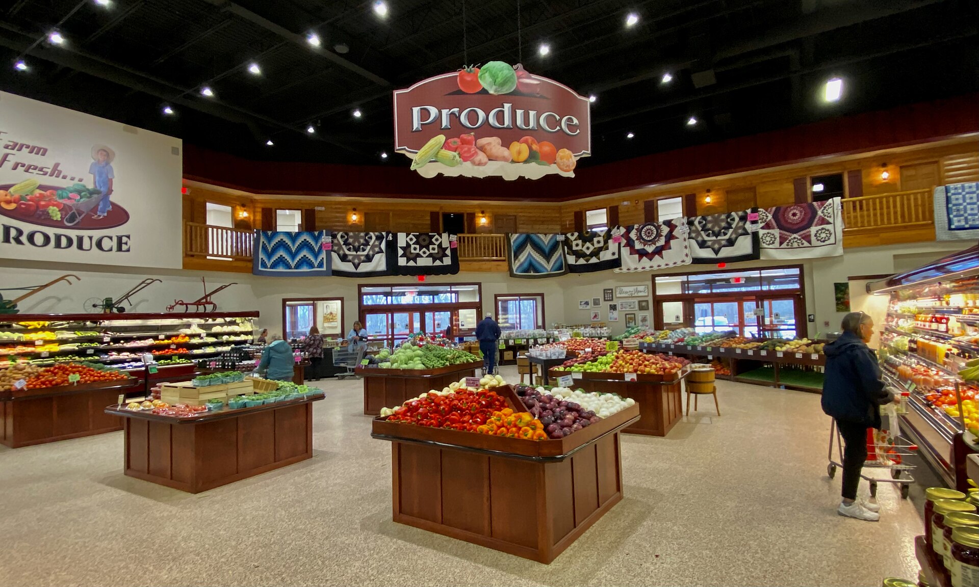 Sección de frutas y verduras de un supermercado, con mesas de pimientos, manzanas y cebollas bajo un cartel que dice Produce