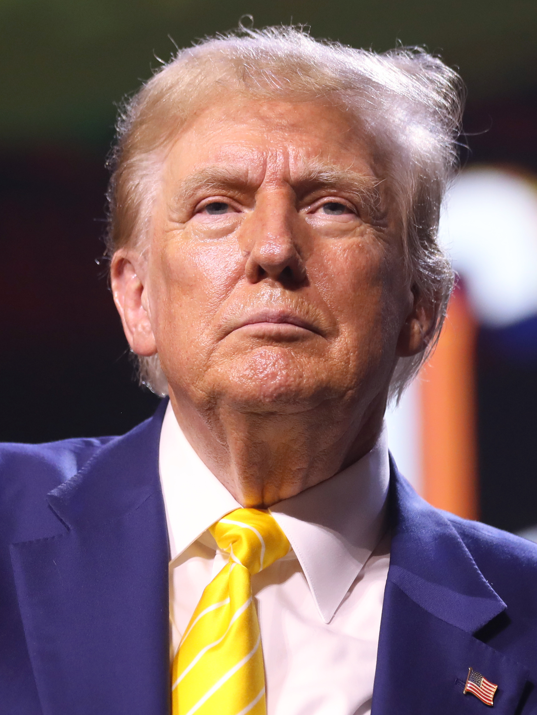 Donald Trump con traje azul, camisa blanca y corbata amarilla, durante un mitin