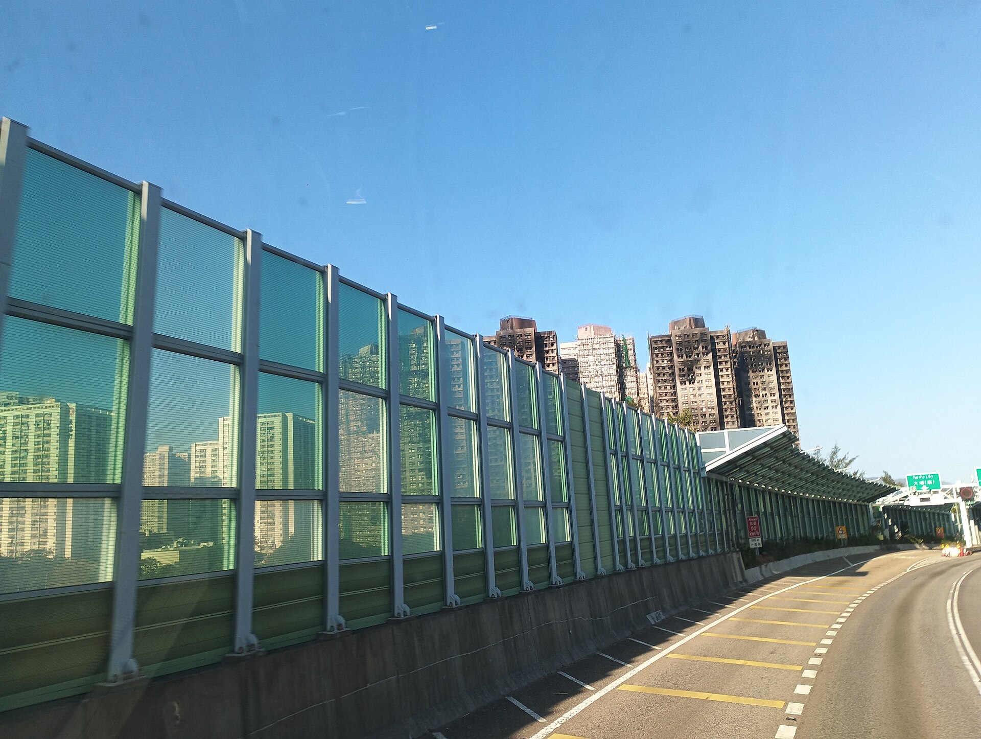 Fire-blackened residential towers seen in the distance from a highway with green noise barriers