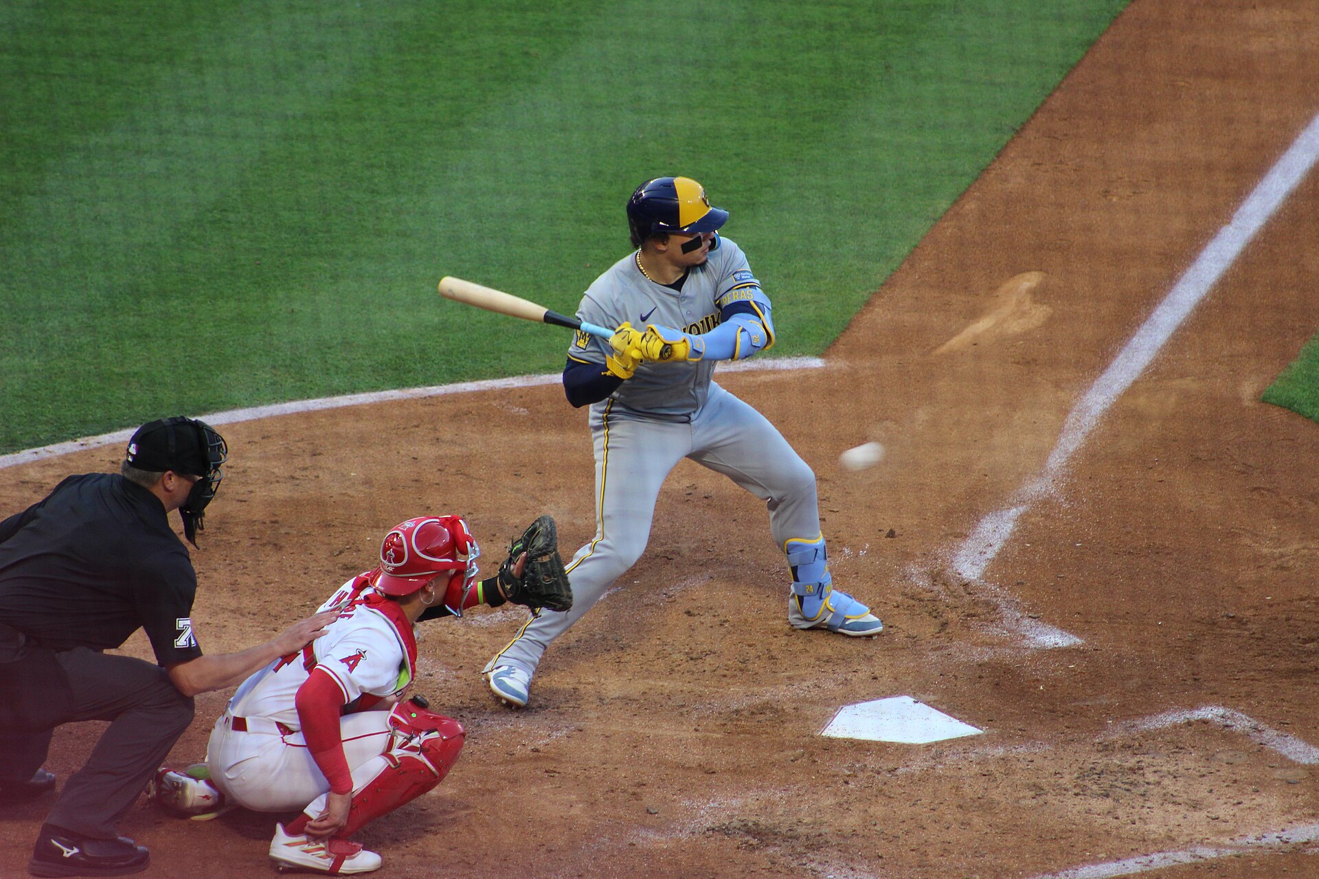 William Contreras at bat in the Brewers' grey uniform, with the opposing catcher and the umpire behind him