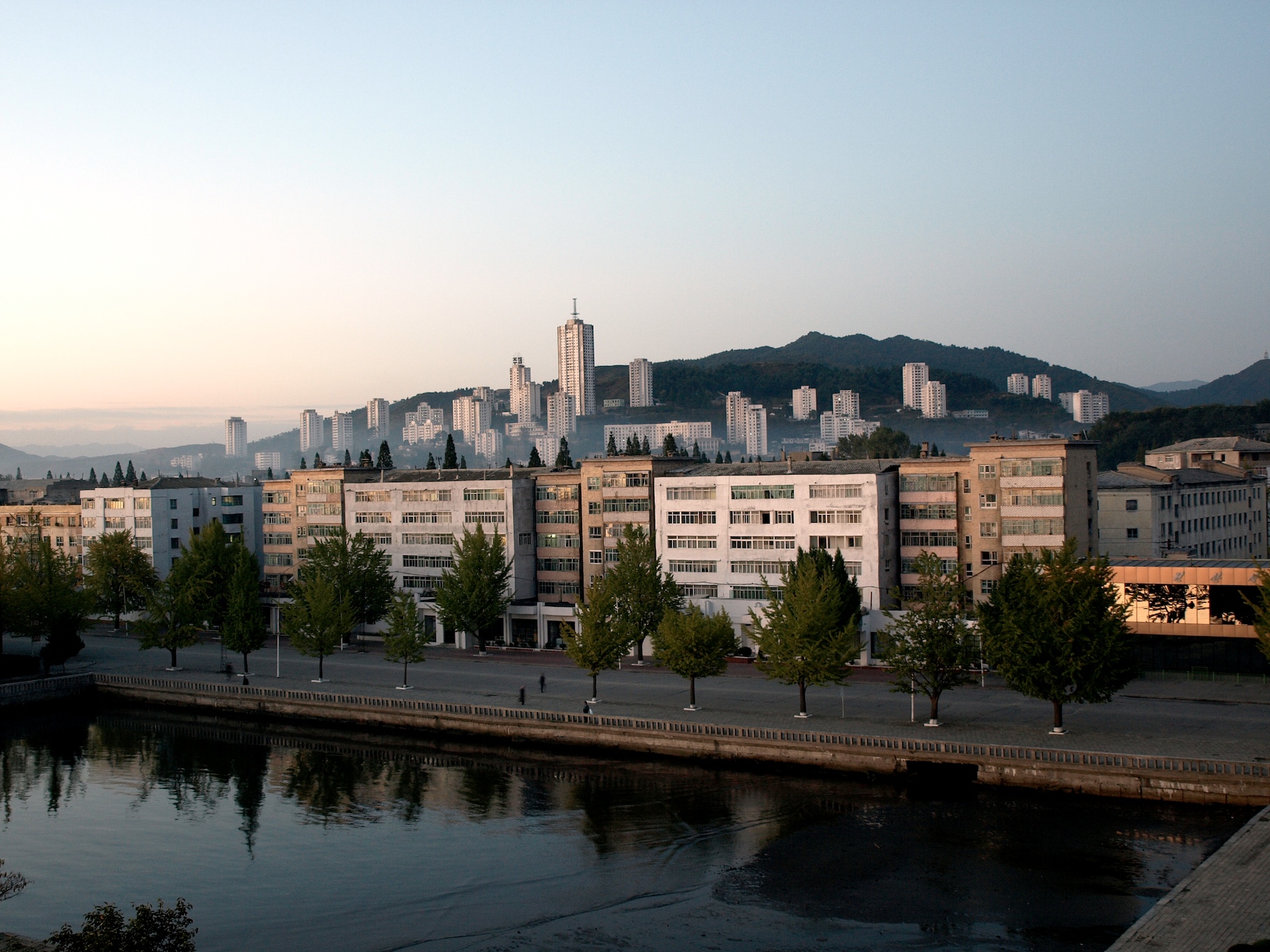 Edificios de viviendas junto a un canal en la ciudad de Wonsan, con rascacielos y montañas al fondo al atardecer